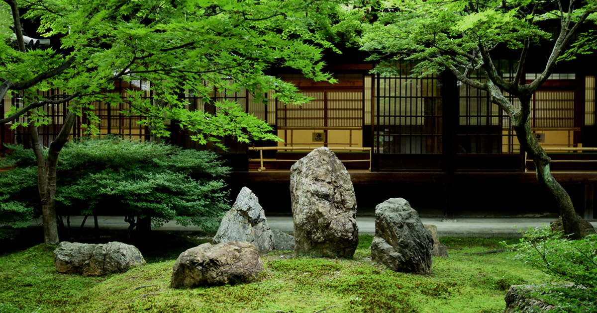新緑が美しい日本庭園。苔庭に配された石組と、障子戸を備えた伝統的な和建築が調和する静かな空間。