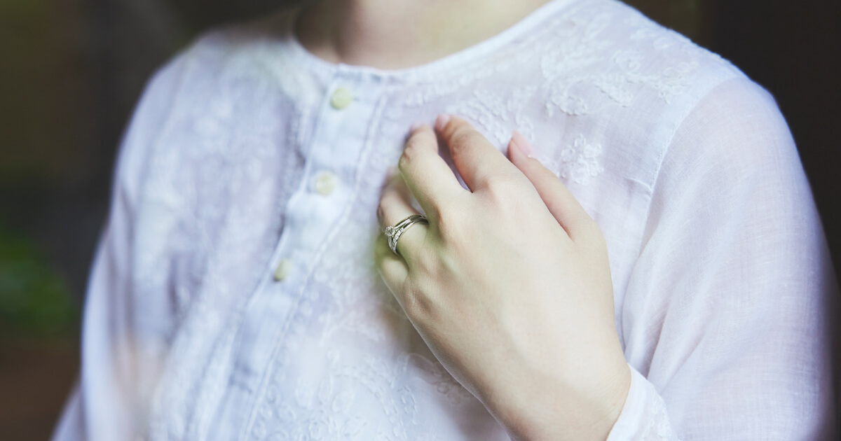 白いブラウスを着用した女性の手元に、AMATSUの婚約指輪と結婚指輪を重ね着けしたイメージ。繊細なダイヤモンドの輝きと上品なデザインが手元を美しく彩るブライダルリング。
