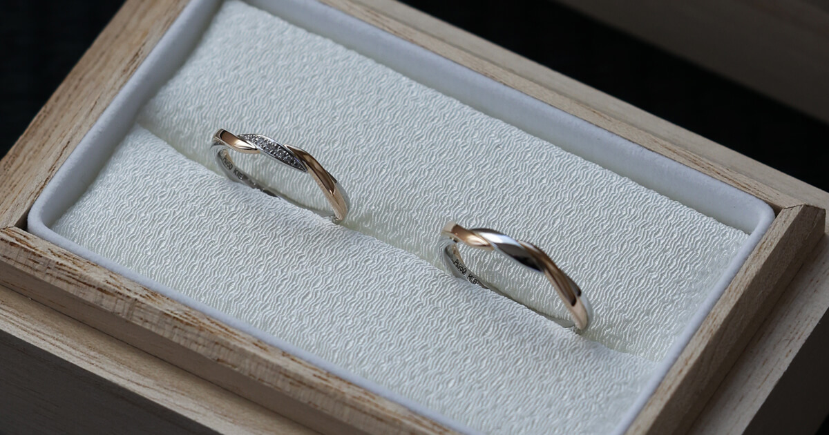木製のリングボックスに収められた、緩やかな曲線が重なり合うAMATSUの結婚指輪