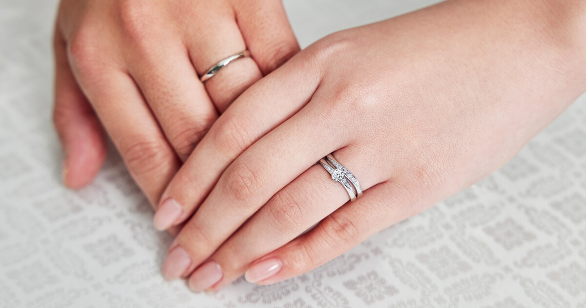 AMATSU「波 -nami-」の婚約指輪と結婚指輪。穏やかな波を思わせる流れるような曲線が、おふたりの手元に寄り添い、美しく重なり合うブライダルリング。