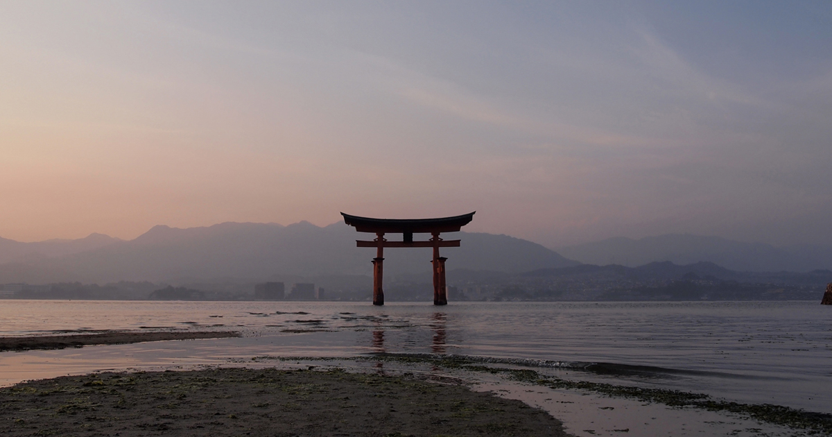 薄明の空の下、穏やかな瀬戸内海に佇む宮島の大鳥居